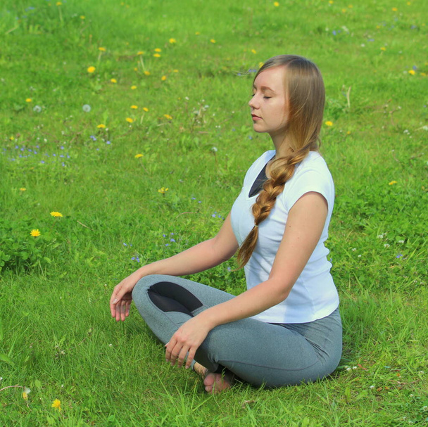 Young woman of European appearance does yoga in summer nature. Woman sitting in easy pose, sukhasana. High quality photo for web and print with empty space for text and design. - Foto, imagen