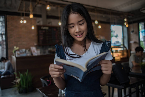 Junge Frau liest Buch im Innenraum eines städtischen Cafés. - Foto, Bild