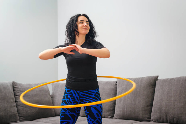Woman rotating hula hoop. Girl training at home. Healthy sporty lifestyle. Woman doing workout and works with hula hoop. Happy fitness woman. Waist building and weight loss concept. - 写真・画像