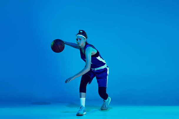 Young caucasian female basketball player isolated on blue studio background in neon light - Фото, изображение