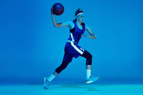 Young caucasian female basketball player isolated on blue studio background in neon light - Fotó, kép