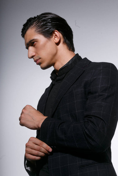 Gros plan portrait d'un beau jeune homme sérieux en costume noir sur fond blanc foncé. Vue verticale. - Photo, image