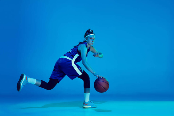 Young caucasian female basketball player isolated on blue studio background in neon light - Foto, Imagen