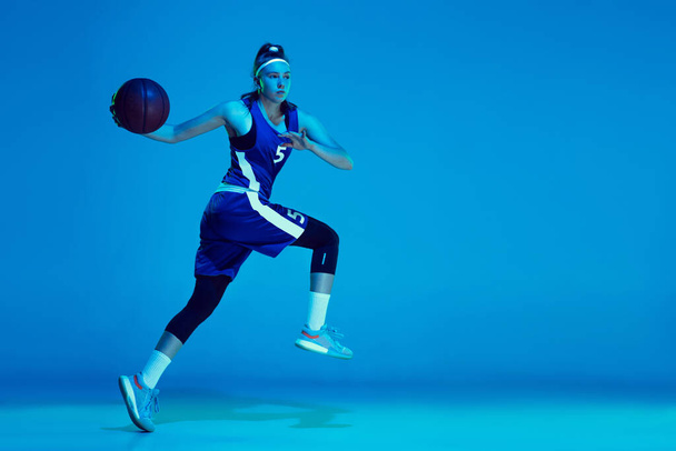 Joven jugador de baloncesto femenino caucásico aislado en fondo estudio azul en luz de neón
 - Foto, Imagen