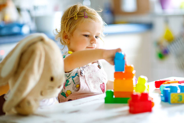 Roztomilé batole dívka s oblíbeným plyšovým králíček hrát s vzdělávací hračky v jeslích. Šťastné zdravé dítě baví s barevné různé plastové bloky doma. Roztomilé dítě učení vytváření. - Fotografie, Obrázek