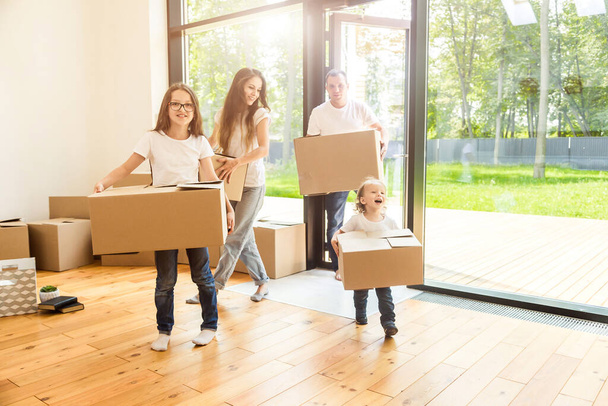 Happy young family, parents daughter and son, unpacking boxes and moving into a new home. funny kids run in with boxes - Foto, Bild