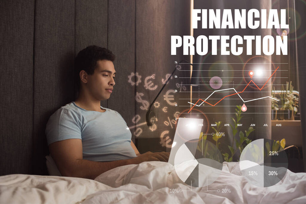 handsome mixed race freelancer using laptop near financial protection lettering, money signs, charts and graphs   - Photo, Image