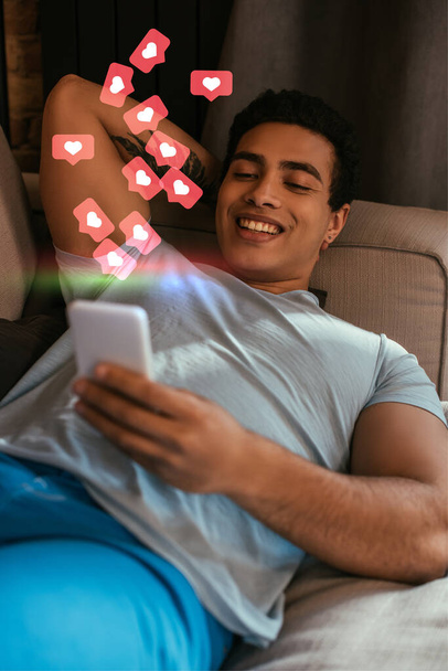 foco seletivo de homem de raça mista refrigeração e usando smartphone perto de corações virtuais
  - Foto, Imagem