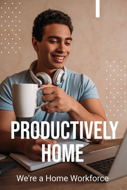 gelukkig gemengd ras man met koffiebeker tijdens het schrijven in de buurt van laptop en productief thuis, waren een thuiswerkers belettering  - Foto, afbeelding