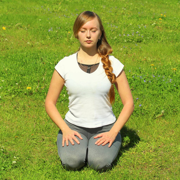 Young woman of European appearance does yoga in summer nature. Woman sitting on her knees in vajrasana, thunderbolt pose. High quality photo for web and print with empty space for text and design. - Фото, изображение