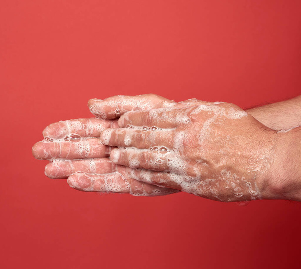 δύο αρσενικά χέρια σε ένα λευκό σαπουνόφουσκας αφρό, υγιεινή του σώματος, κόκκινο φόντο  - Φωτογραφία, εικόνα