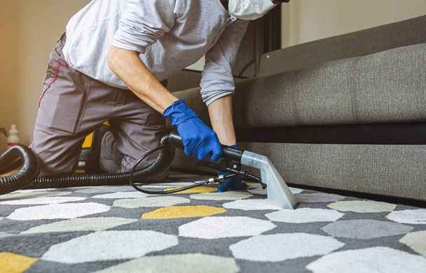 Male worker removing dirt from carpet with professional vacuum cleaner indoors - Foto, Imagen