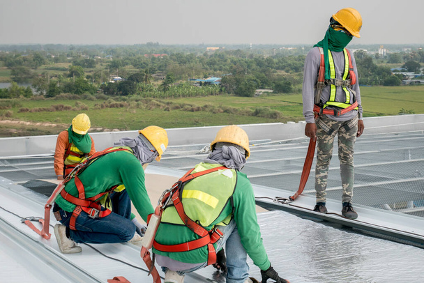 Bauarbeiter mit Sicherheitsgurt und Sicherheitsleine arbeiten auf dem Dach einer neuen Lagerhalle der Metallindustrie - Foto, Bild