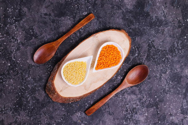 Raw orange lentils and yellow millet for proper nutrition and health in white plates on a wooden stand with wooden spoons on a gray background - Photo, Image