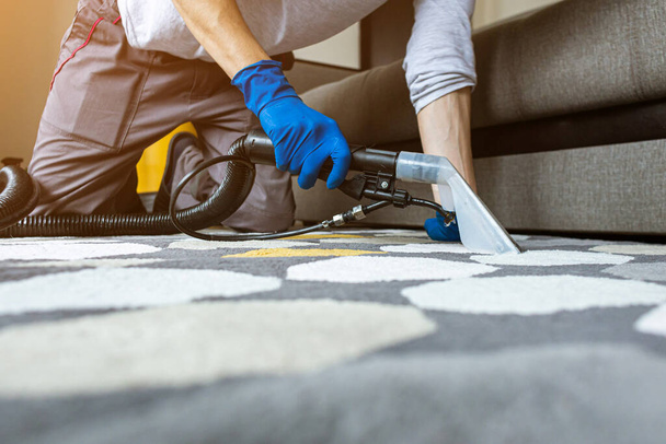 Male worker removing dirt from carpet with professional vacuum cleaner indoors - Photo, image