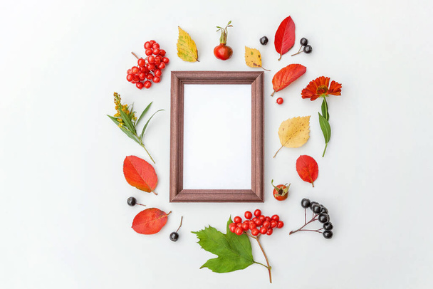 Autumn floral composition. Vertical frame mockup chokeberry rowan berries colorful leaves dogrose flowers on white background. Fall natural plants ecology concept. Flat lay top view copy space - Photo, image