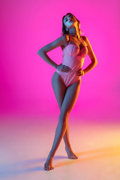 Beautiful girl in fashionable swimsuit isolated on gradient studio background in neon light. Summer, resort, fashion and weekend concept - Fotoğraf, Görsel
