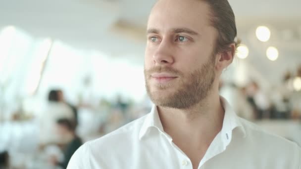 A close-up view of an attractive young businessman is looking to the camera in a city cafe indoors - Materiał filmowy, wideo