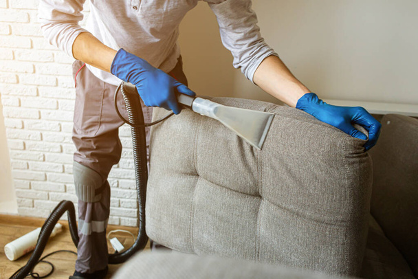Dry cleaners man employee removing dirt from furniture in flat, closeup, vacuum clean sofa with professional equipment. cleaning service. - Fotó, kép