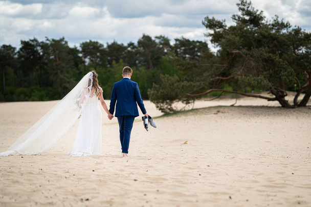 A landscape shot of a couple walking on sand on their wedding day - Foto, Imagem