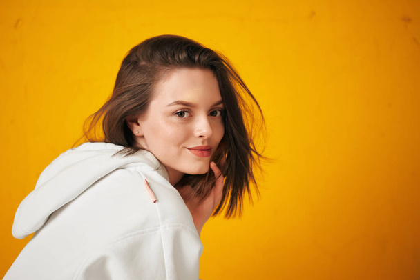 Portrait of a young pretty female student in a white hoodie, casual clothing against a concrete orange wall. - Foto, Bild