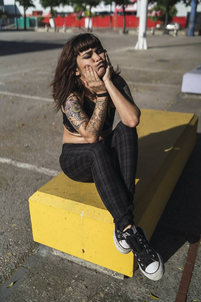 A young attractive Caucasian female with tattoos sitting in the street - Fotoğraf, Görsel