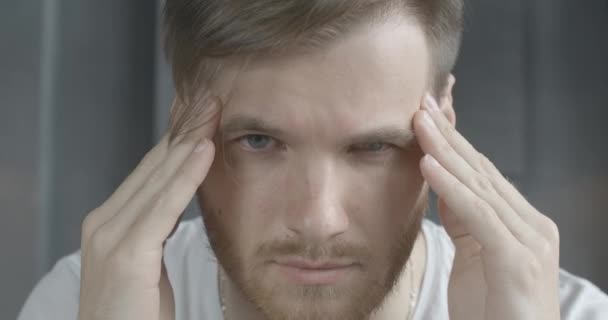 Extreme close-up of brunette Caucasian man with grey eyes rubbing temples. Portrait of young handsome bearded guy having severe headache. Health care, overworking, stress, tension. Cinema 4k ProRes HQ - Кадры, видео