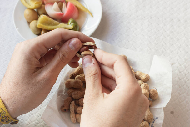 eine Hand, die Erdnüsse von einem Teller neben einem Oliventeller schält - Foto, Bild
