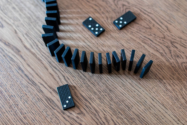 zwarte dominocards met witte stippen in rijen en uitgebalanceerd op een houten tafel. Tegels van de domino voordat vallen voor een ketting effect. Bedrijfsrampenconcept met domino-effect - Foto, afbeelding