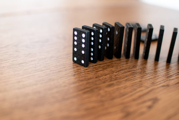 黒いドミノカードに白い点が連続して木製のテーブルの上で次々にバランスをとる。チェーン効果のために落ちる前にドミノのタイル。ドミノ効果で事業災害の概念 - 写真・画像