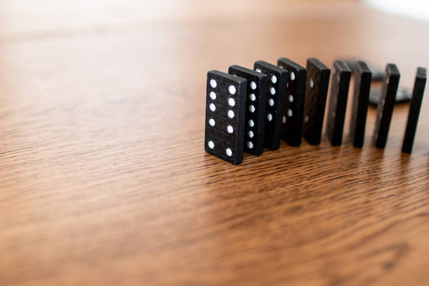 czarne domino karty z białymi kropkami w rzędach i zrównoważony jeden po drugim na drewnianym stole. Płytki domina przed zakochaniem się w efekt łańcucha. Koncepcja katastrofy biznesowej z efektem domina - Zdjęcie, obraz