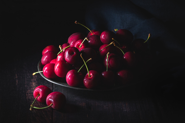 Темно-красные вишни на оловянной тарелке. Низкий свет, горизонтальный состав
. - Фото, изображение