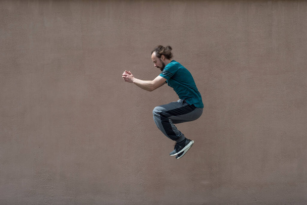 young bearded guy sortsman jumping on the background of a pink street wall. Portrait of a bearded guy of thirty years old, in sportswear, jumping high against a textured pink street wall. Active lifestyle, sport, young guy jumping, high jump, save sp - Фото, изображение