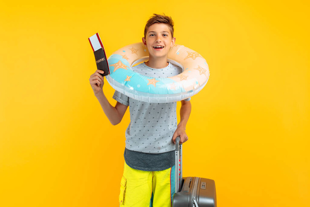 adolescente feliz está parado con una maleta y un círculo inflable del mar aislado sobre un fondo amarillo. Concepto de vacaciones de verano, viajes
 - Foto, imagen