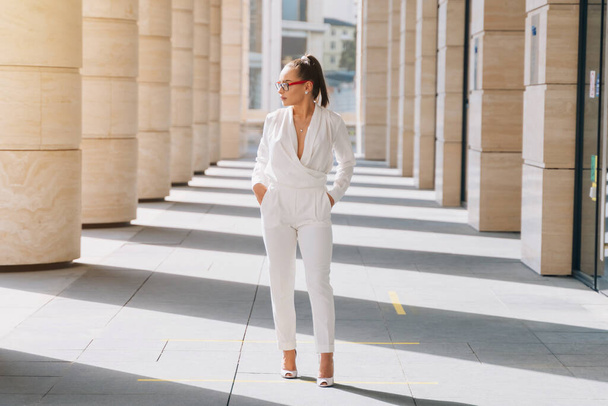 Stylish girl in a white expensive suit with beautiful glasses. Kavkah model Stands posing for Photographer. - Фото, зображення