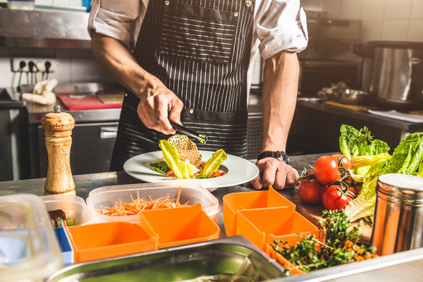 Professional chef cooking in the kitchen restaurant at the hotel, preparing dinner. A cook in an apron makes a salad of vegetables and pizza. - 写真・画像