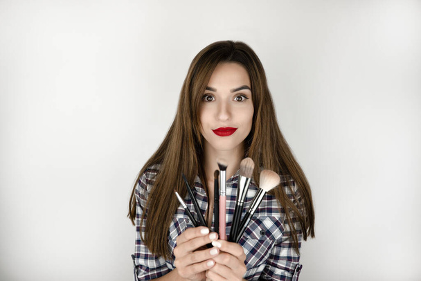 brunette young woman with red lips holding makeup brushes in both hands , beauty and style, isolated white background. - Фото, изображение