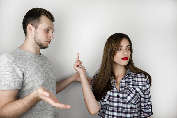 young couple handsome man and beautiful woman quarrelling on isolated white background, she shows him fuck off sign , relationships problem concept. - Photo, image