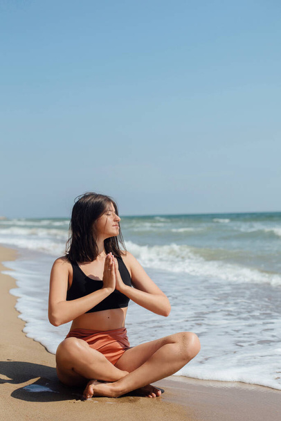 Йога и медитация на пляже. Молодая красивая женщина практикует йогу, сидит на берегу моря и медитирует. Концепция психического здоровья и ухода за собой. Летний отдых
 - Фото, изображение