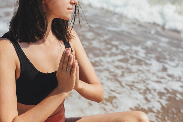 Yoga e meditação na praia. Vista cortada da jovem mulher bonita praticando ioga, sentado na praia e meditando no mar. Conceito de saúde mental e autocuidado. Férias
 - Foto, Imagem