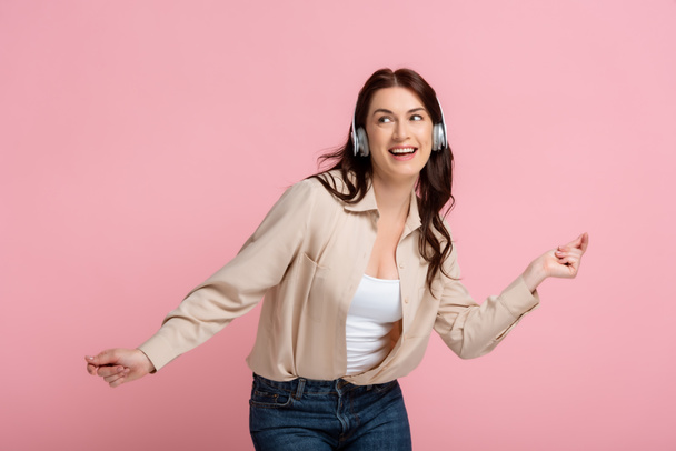 Smiling woman in headphones dancing isolated on pink, concept of body positive  - Photo, Image