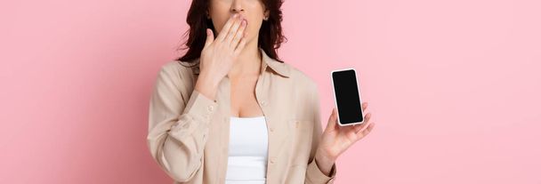 Panoramic crop of shocked woman showing smartphone with blank screen on pink background - Foto, Bild
