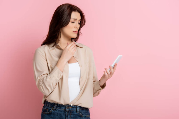 Sad brunette woman using smartphone on pink background, concept of body positive  - Foto, Imagen