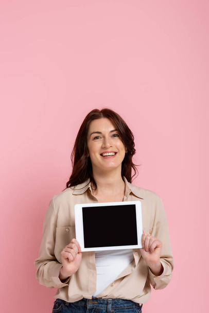 Beautiful smiling woman holding digital tablet with blank screen on pink background - Photo, Image