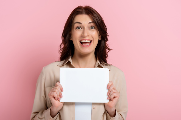 Positive woman looking at camera while holding empty card on pink background - Fotó, kép