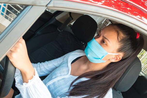 Girl in a medical mask driving a car. Personal protective equipment during the period of coronavirus, epidemic. young woman takes care of her health while travelling - Photo, Image