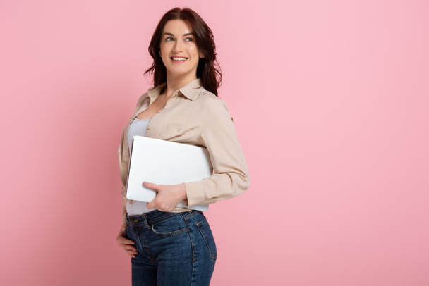 Pozitivní žena s úsměvem pryč při držení notebook na růžovém pozadí, koncept těla pozitivní - Fotografie, Obrázek