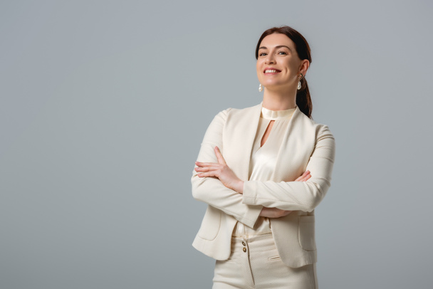 Attractive smiling businesswoman with crossed arms looking at camera isolated on grey  - Foto, imagen