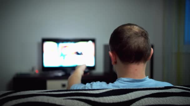 Homem solteiro assistindo TV à noite sentado no sofá, vista traseira
 - Filmagem, Vídeo
