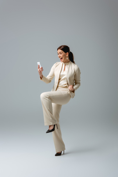 陽気女性でフォーマルウェアショーはいジェスチャーながら使用スマートフォン上の灰色の背景 - 写真・画像